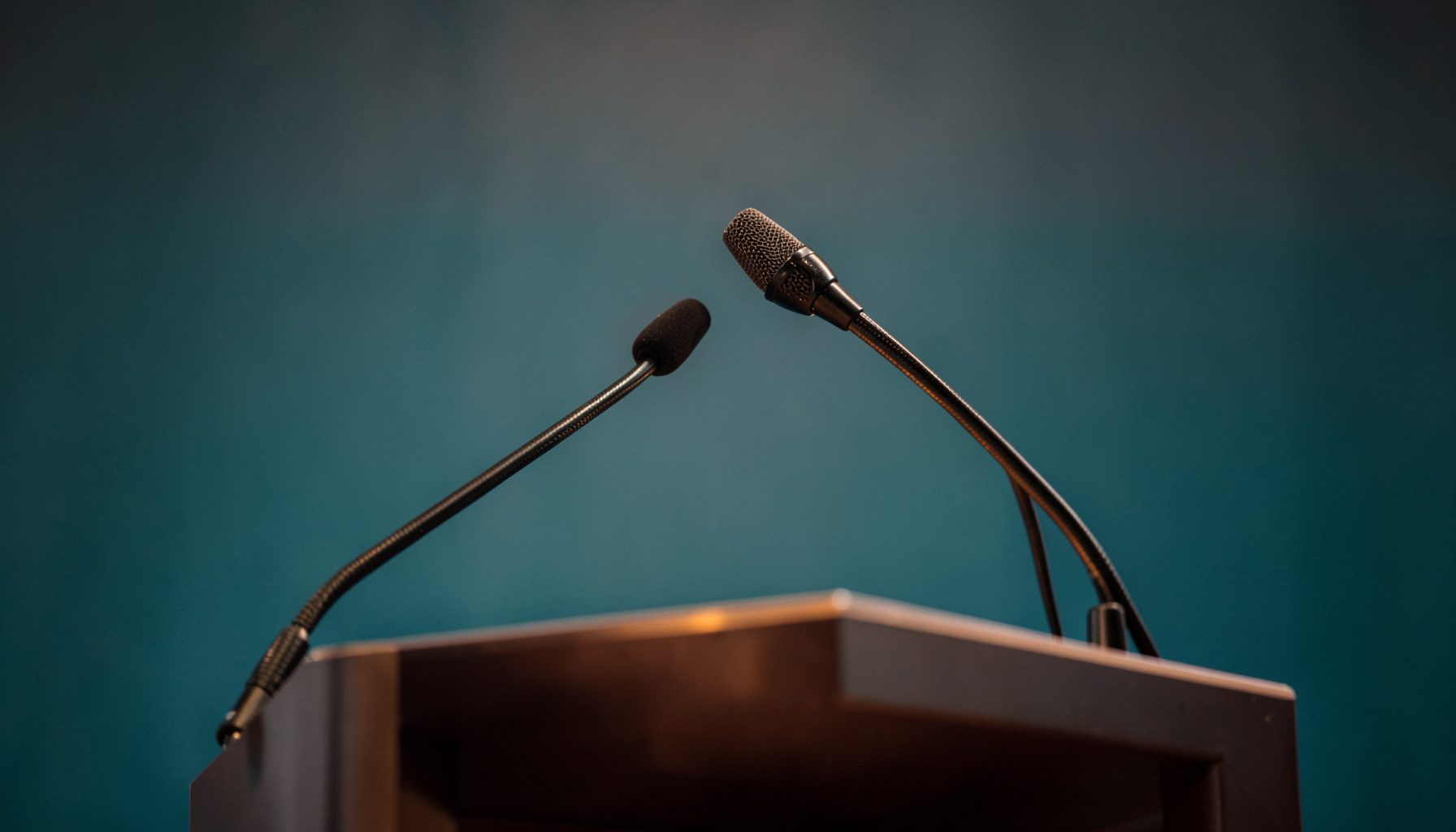 A close-up of a professional conference setting with a podium microphone, soft gray backdrop, and warm ambient lighting